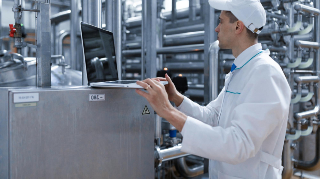 technologist-in-a-white-coat-with-a-laptop-in-his-hands-controls-the-production-process-in-the-dairy-shop-quality-control-at-the-dairy-plant